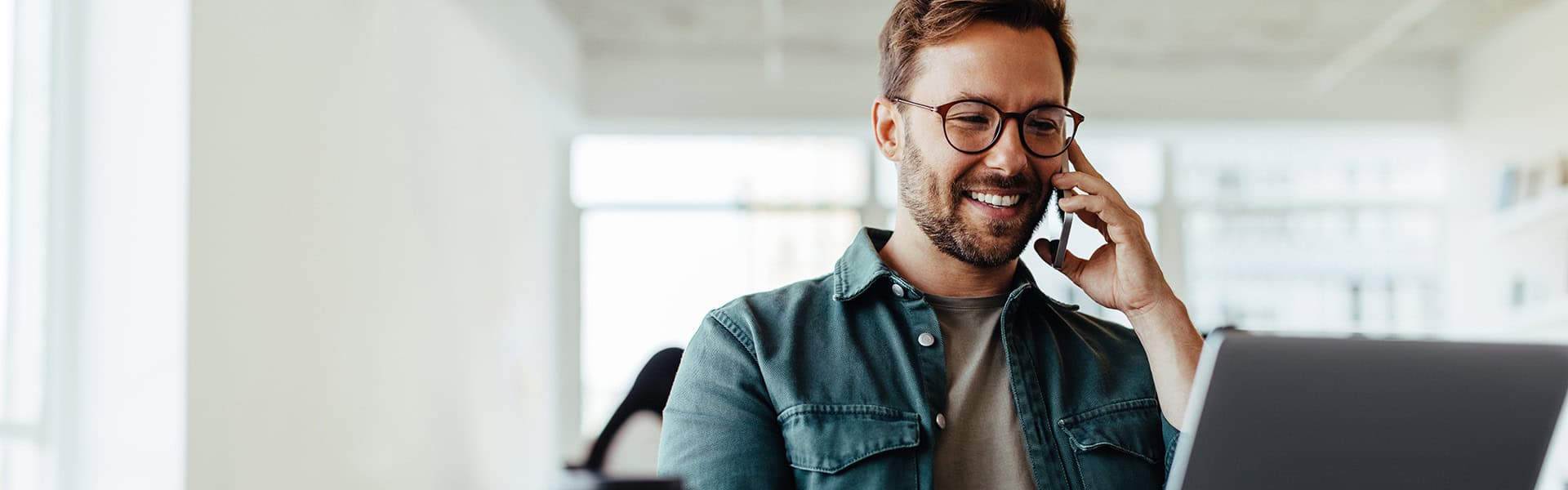 Software designer discussing a new project with his client on the phone. Creative business man working on a laptop in an open plan office / shutterstock.com